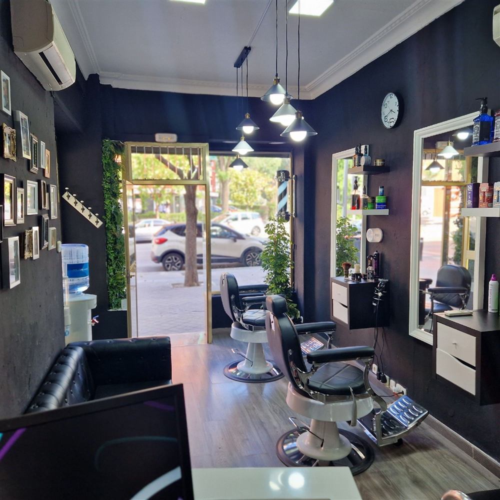 Interior del local: dos sillones de barbero frente a los espejos, paredes negras y lámparas colgantes